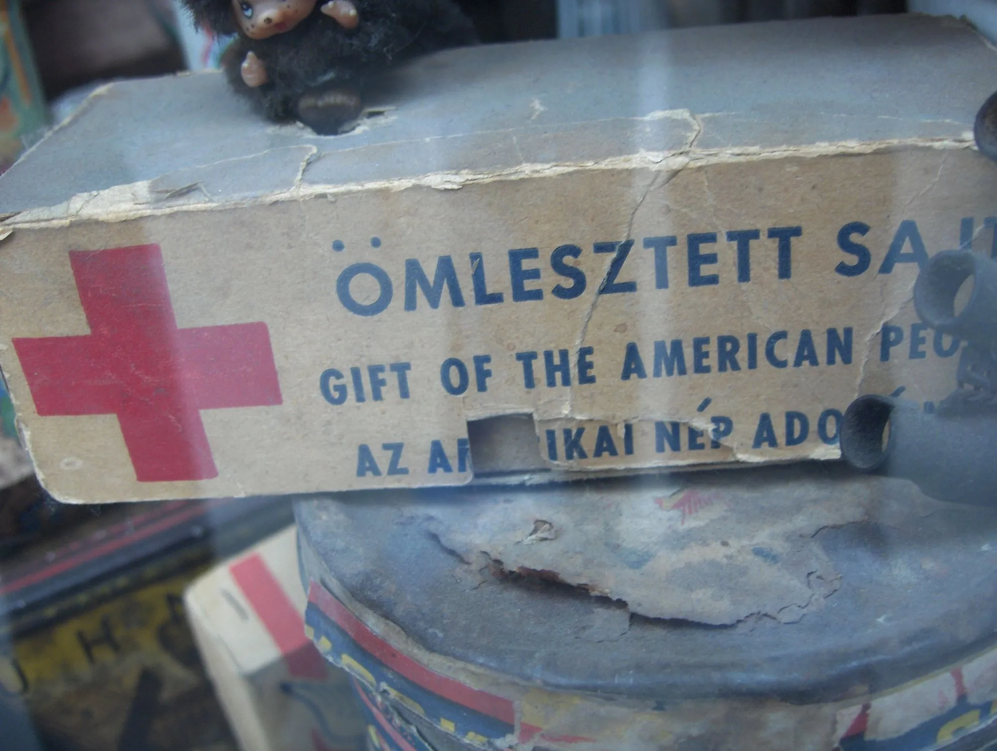 Caja antigua de queso de ayuda de la Cruz Roja con texto en húngaro e inglés, en un escaparate de Budapest