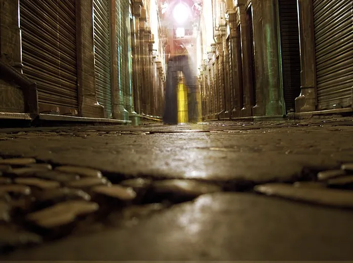 Pasaje comercial de noche con las persianas bajadas, a ras del adoquinado, y una figura en movimiento al fondo