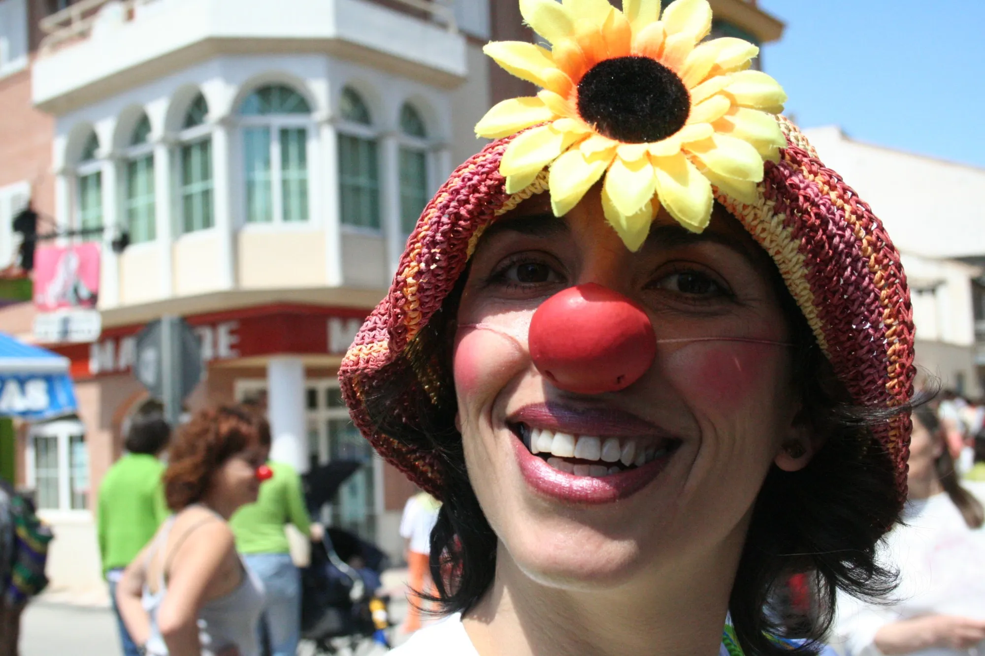 Payasa sonriente con nariz roja y un girasol en el sombrero en una fiesta en la calle