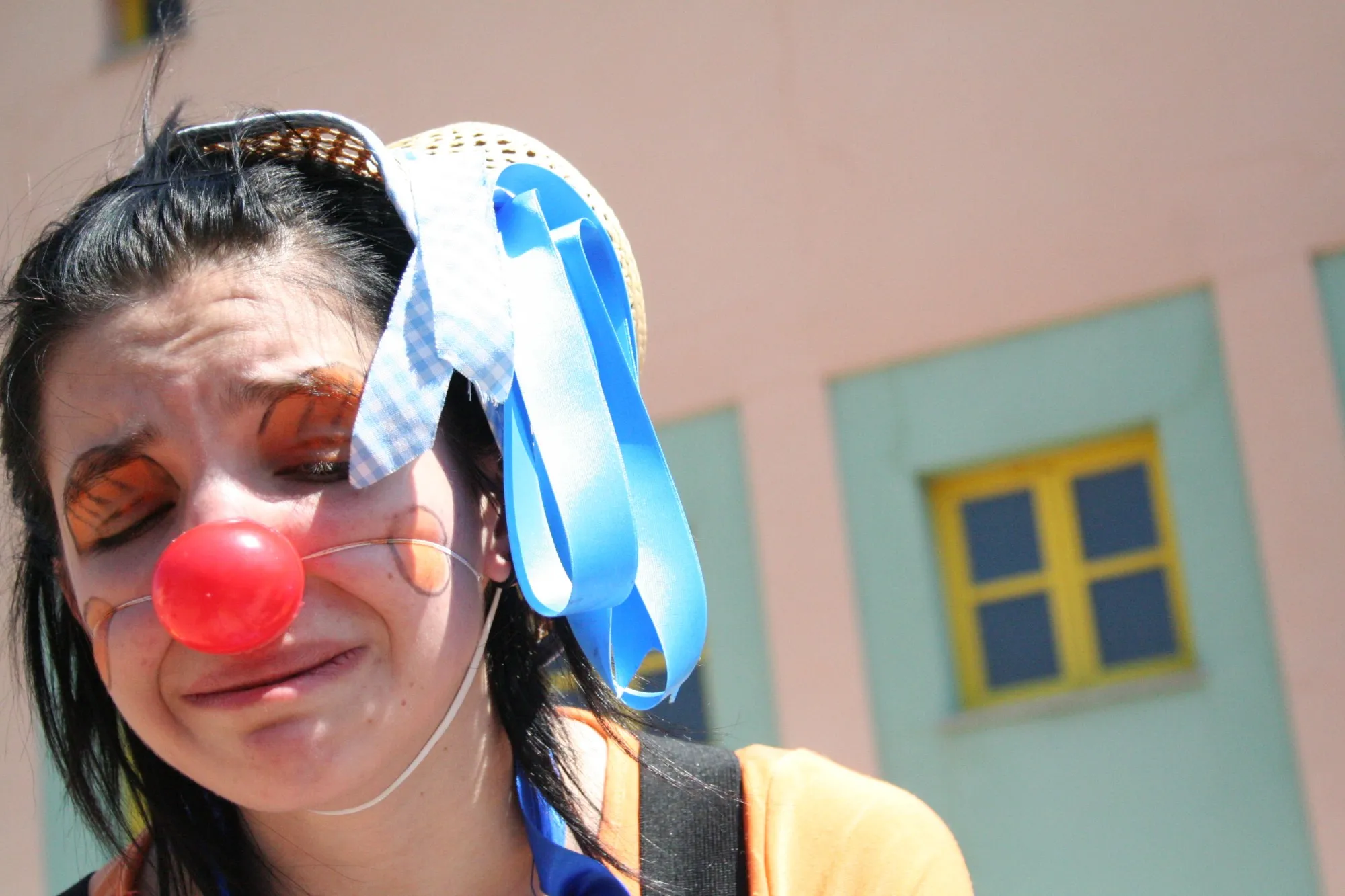 Payasa con nariz roja y lazo azul haciendo un puchero ante una fachada rosa