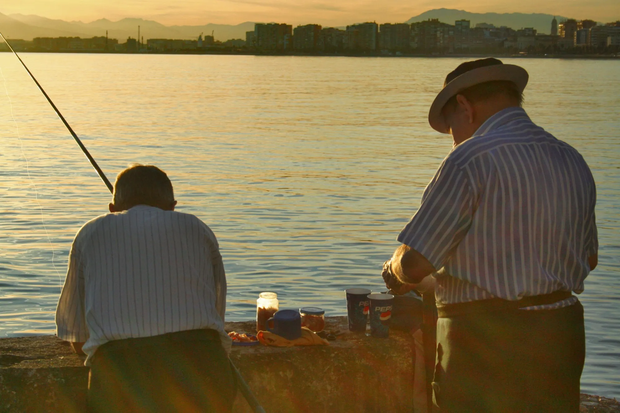 Dos pescadores en el espigón al atardecer con Málaga de fondo