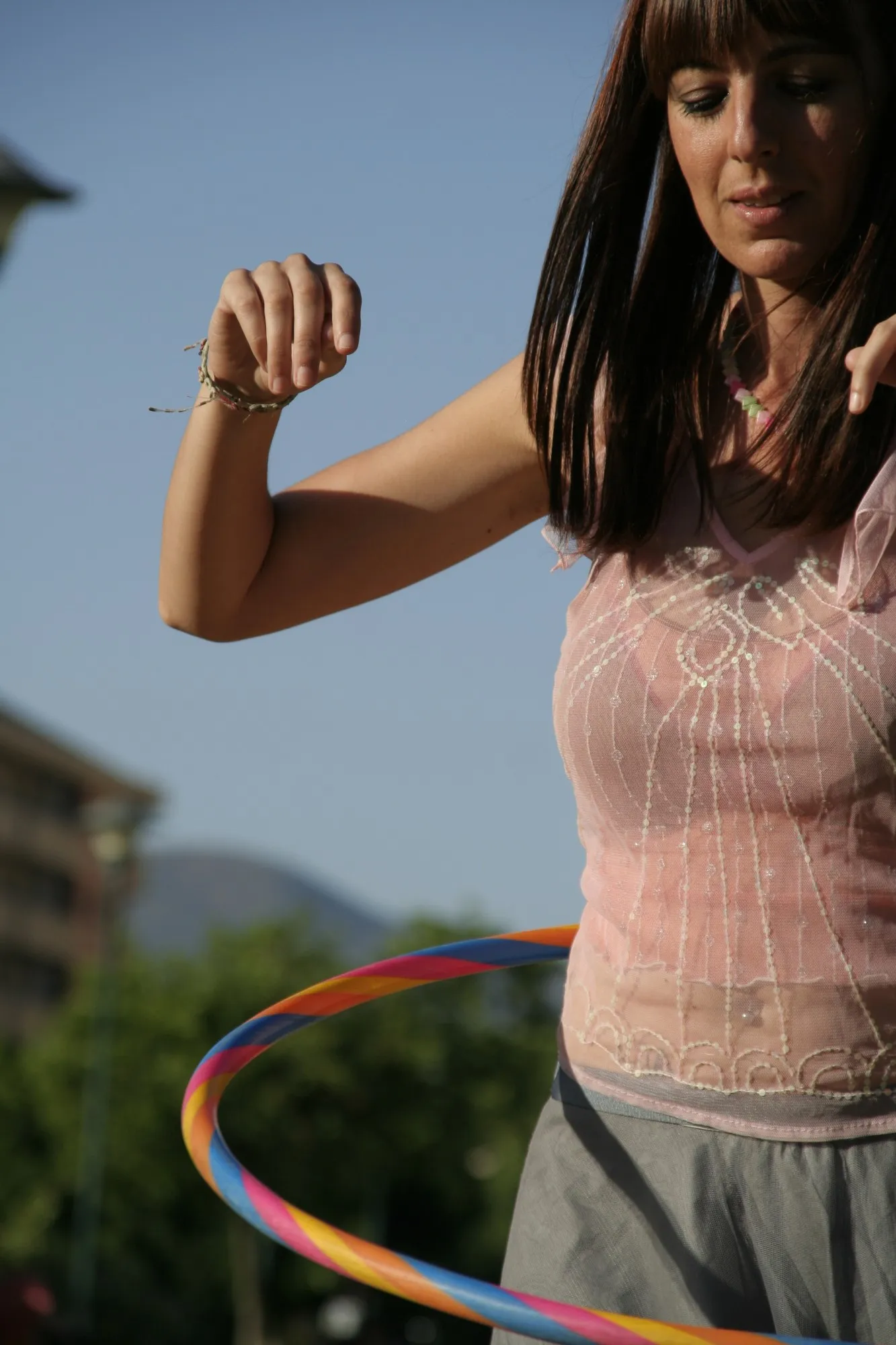 Chica con blusa rosa bailando con un aro de colores bajo el cielo azul