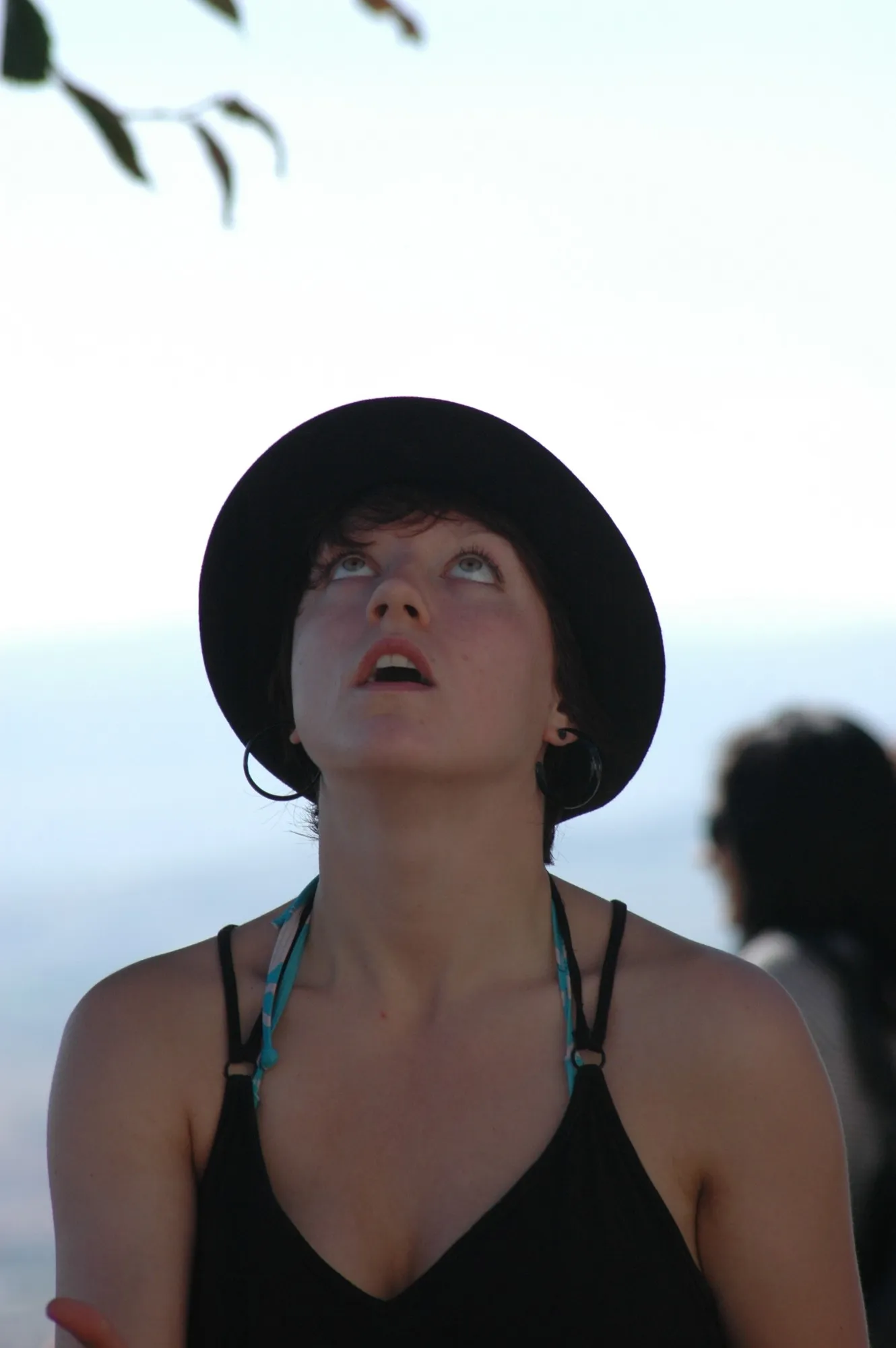 Chica con sombrero negro mirando al cielo, con una rama en primer plano