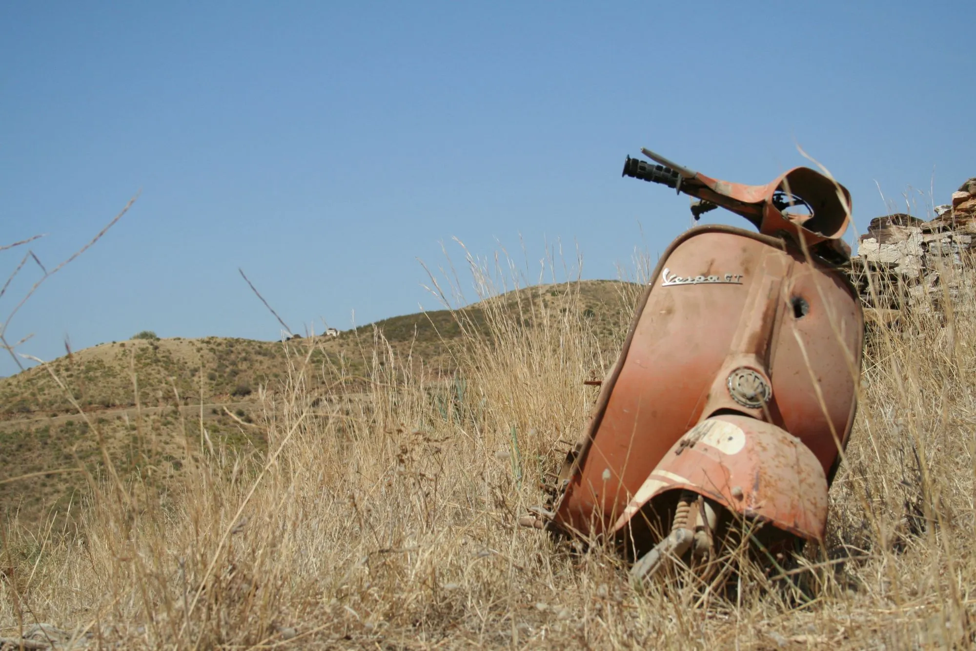 Vespa GT oxidada abandonada entre hierba seca en el campo