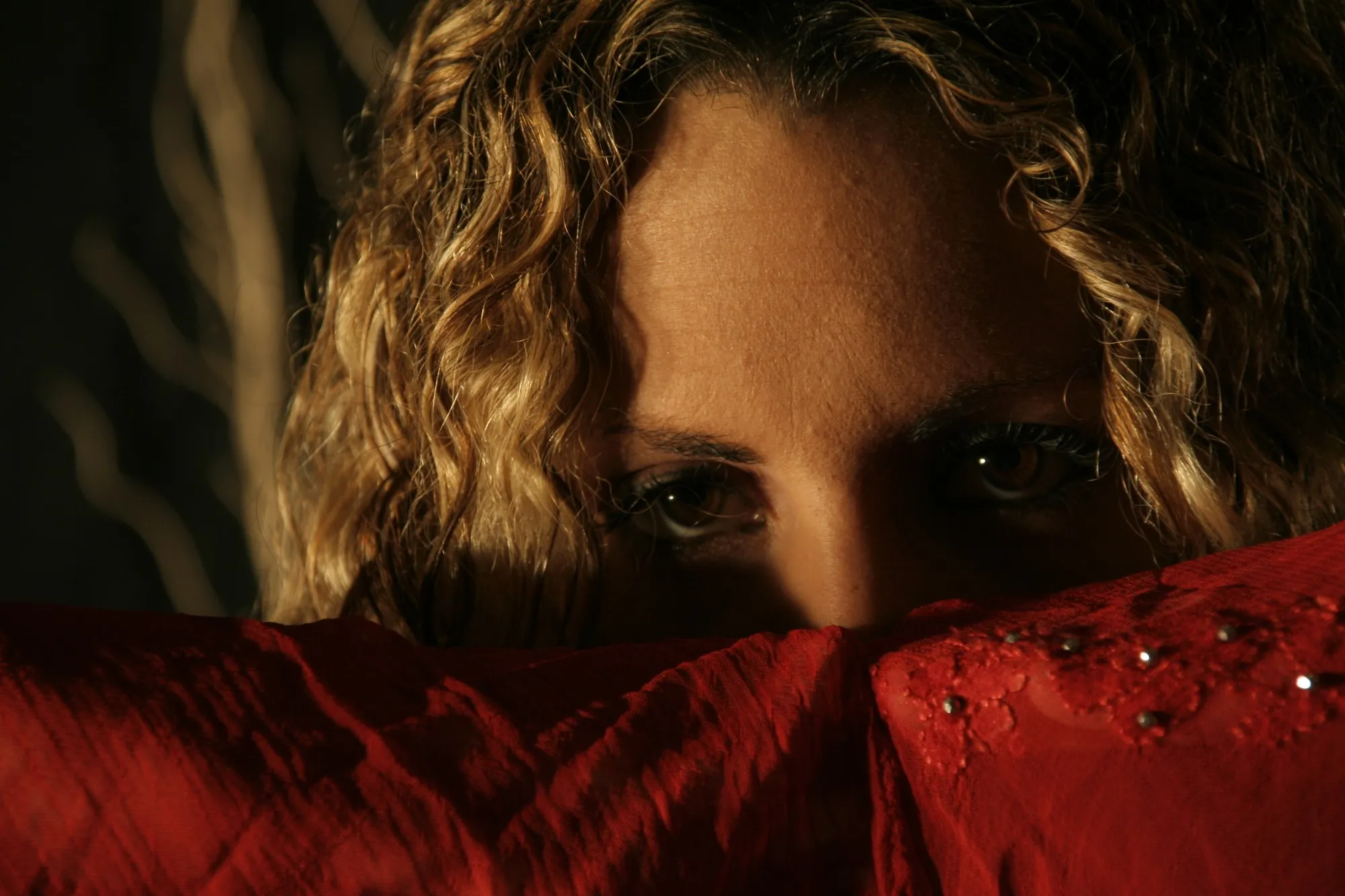 Mirada de una mujer de pelo rizado asomando por encima de una tela roja