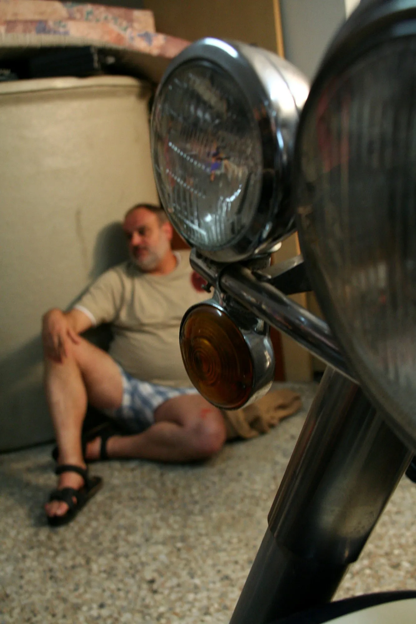 El mismo actor sentado contra la pared, entre los faros y el intermitente de la moto