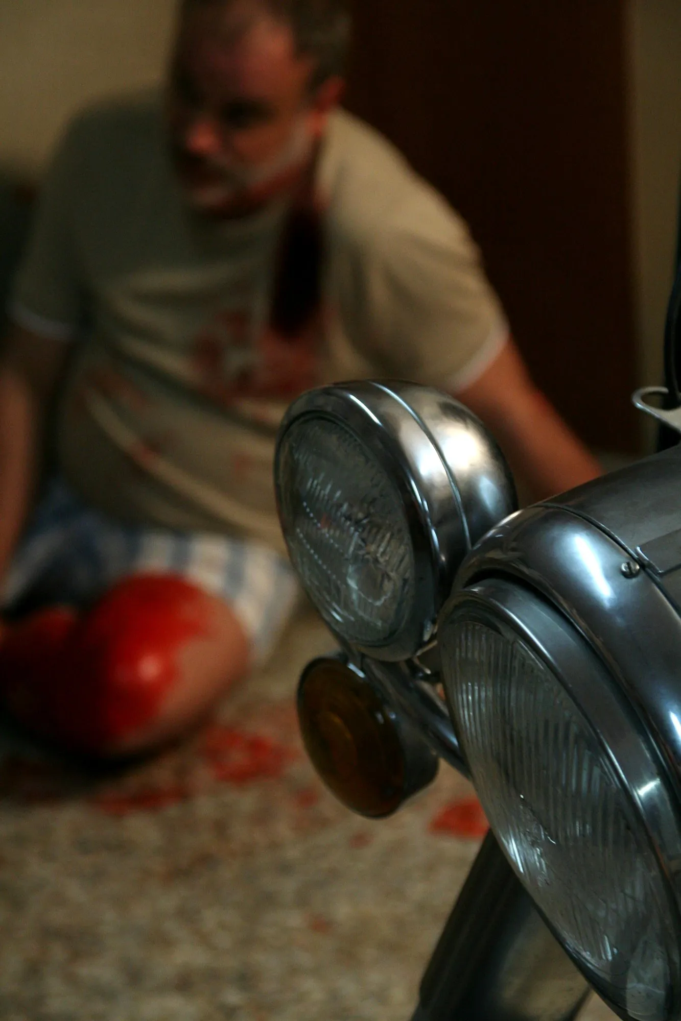 El actor herido sentado en el suelo, desenfocado detrás de los faros cromados de una moto