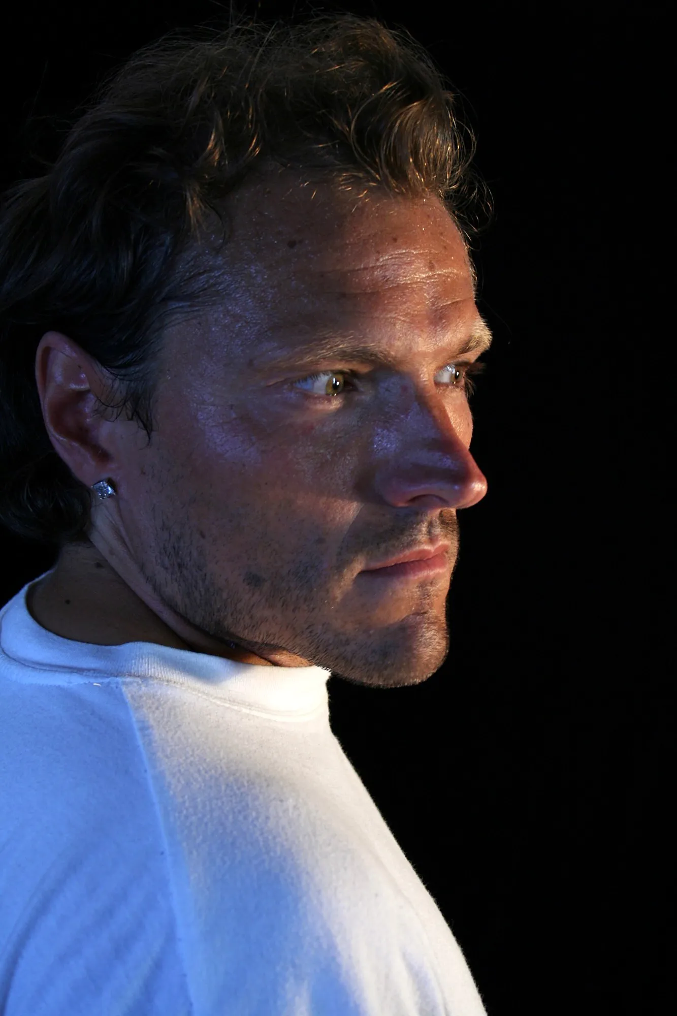 Perfil del mismo actor de camiseta blanca con la luz recortando la cara