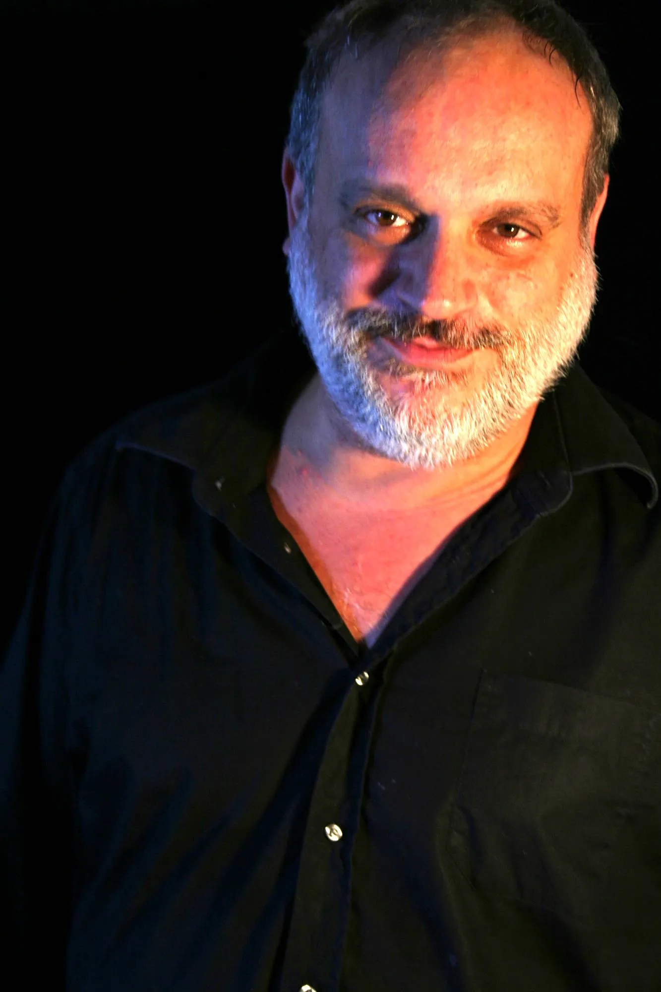 Actor de Granit con barba gris y camisa negra, sonriendo de medio lado