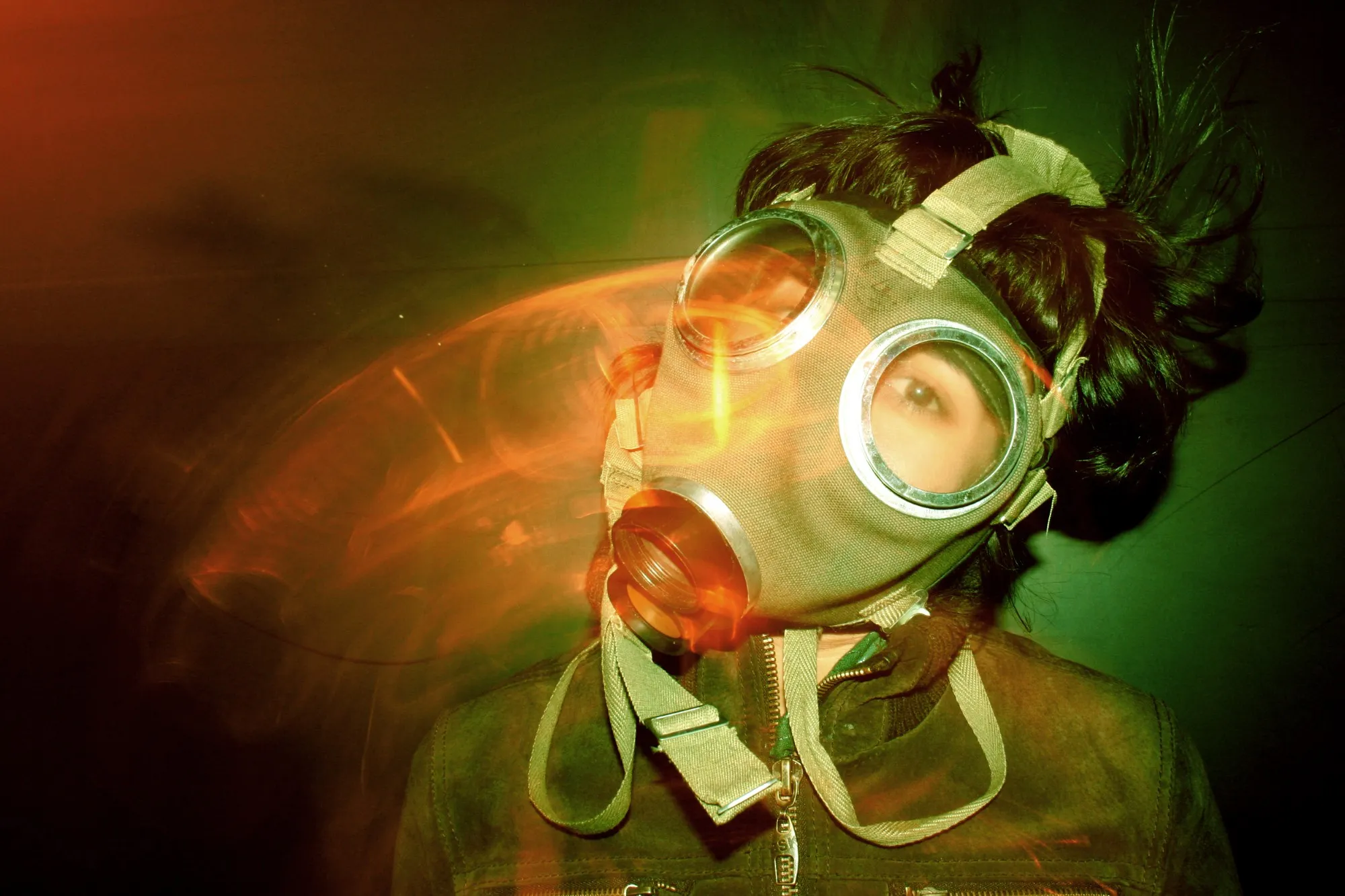 Persona con máscara de gas entre estelas de luz naranja sobre fondo verde