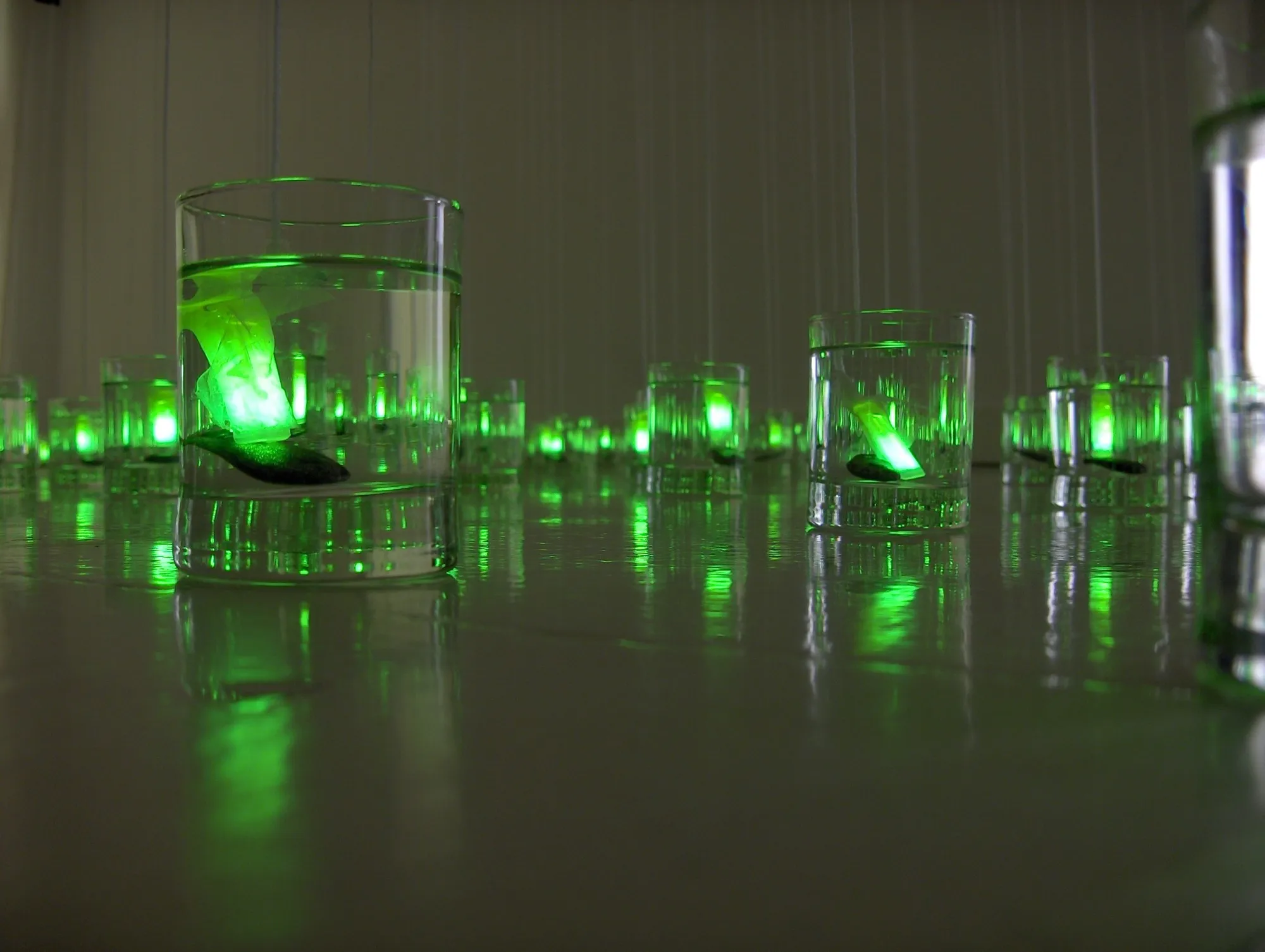 Instalación de vasos de agua con peces y luces verdes reflejados sobre una mesa