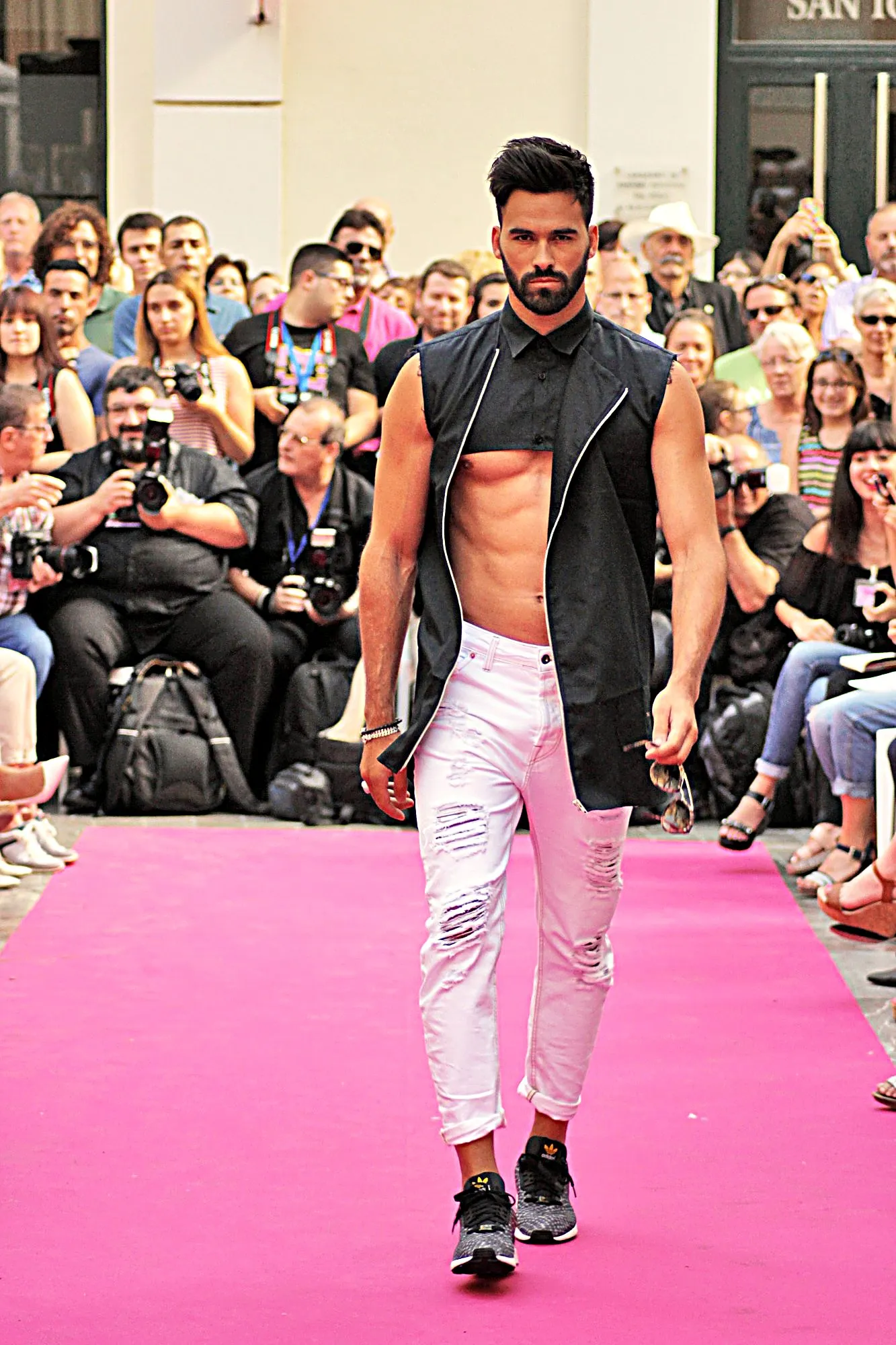 Modelo con chaleco negro abierto con cremallera y vaqueros blancos rotos en la alfombra rosa