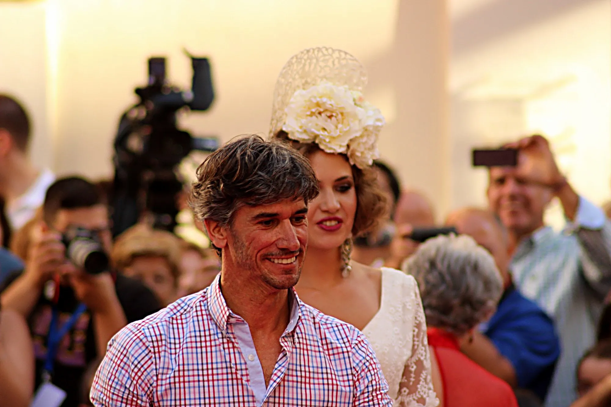 Diseñador sonriendo en la salida final, con una modelo de peineta y flor blanca detrás