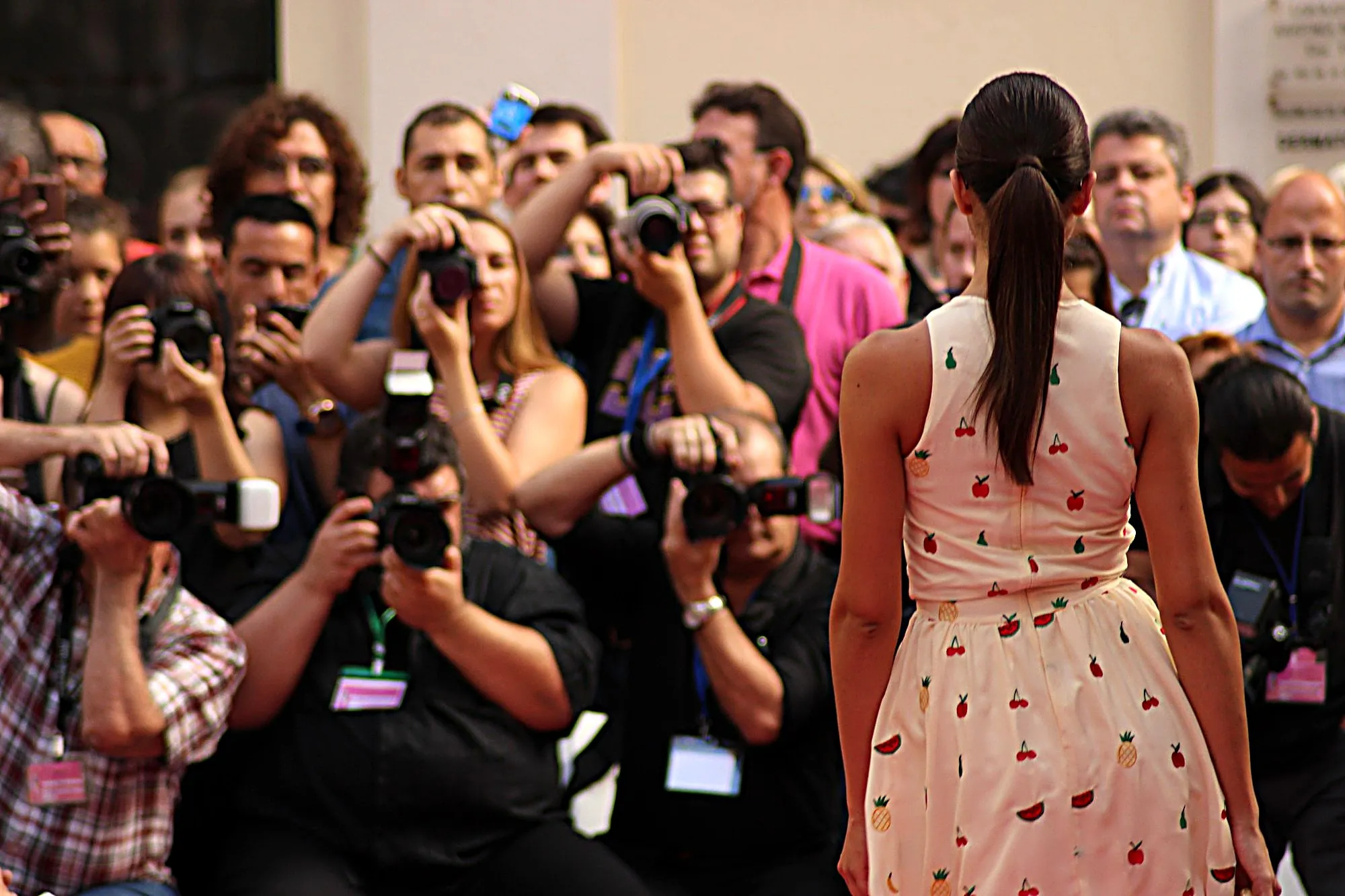 Modelo de espaldas con vestido estampado de frutas, frente a una fila de fotógrafos