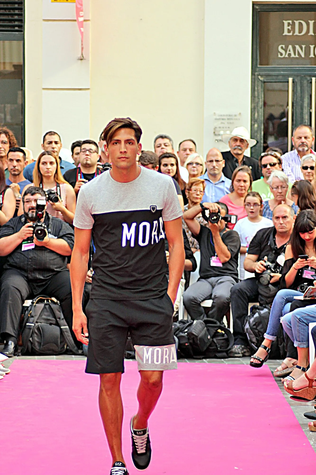 Modelo con camiseta gris y negra y pantalón corto, con los fotógrafos sentados detrás