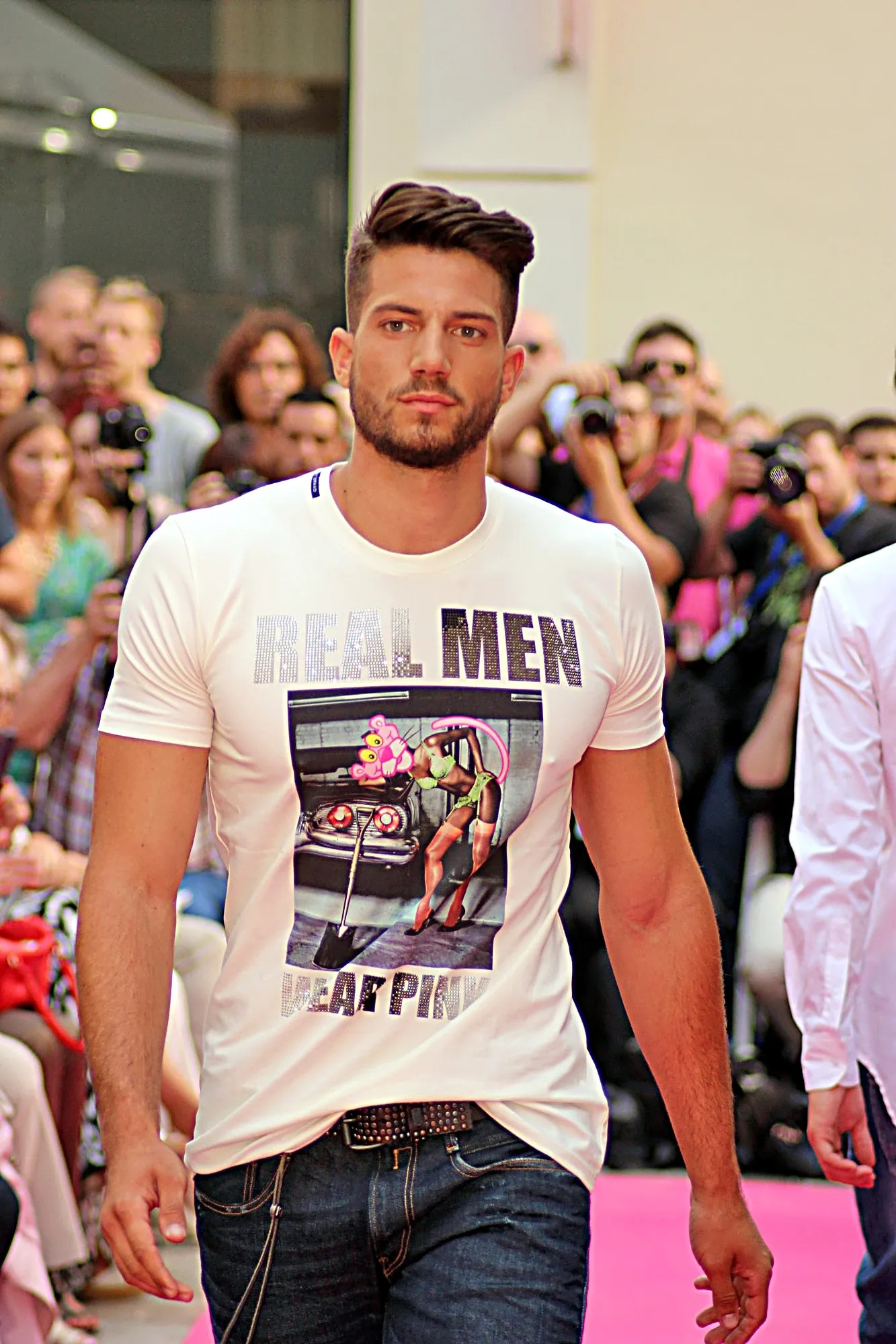 Modelo con barba y camiseta blanca estampada, caminando entre el público