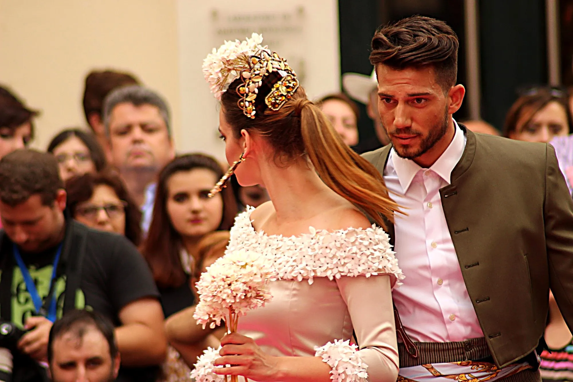 Pareja en la pasarela: ella de flamenca con flores blancas y peina dorada, él con chaquetilla campera