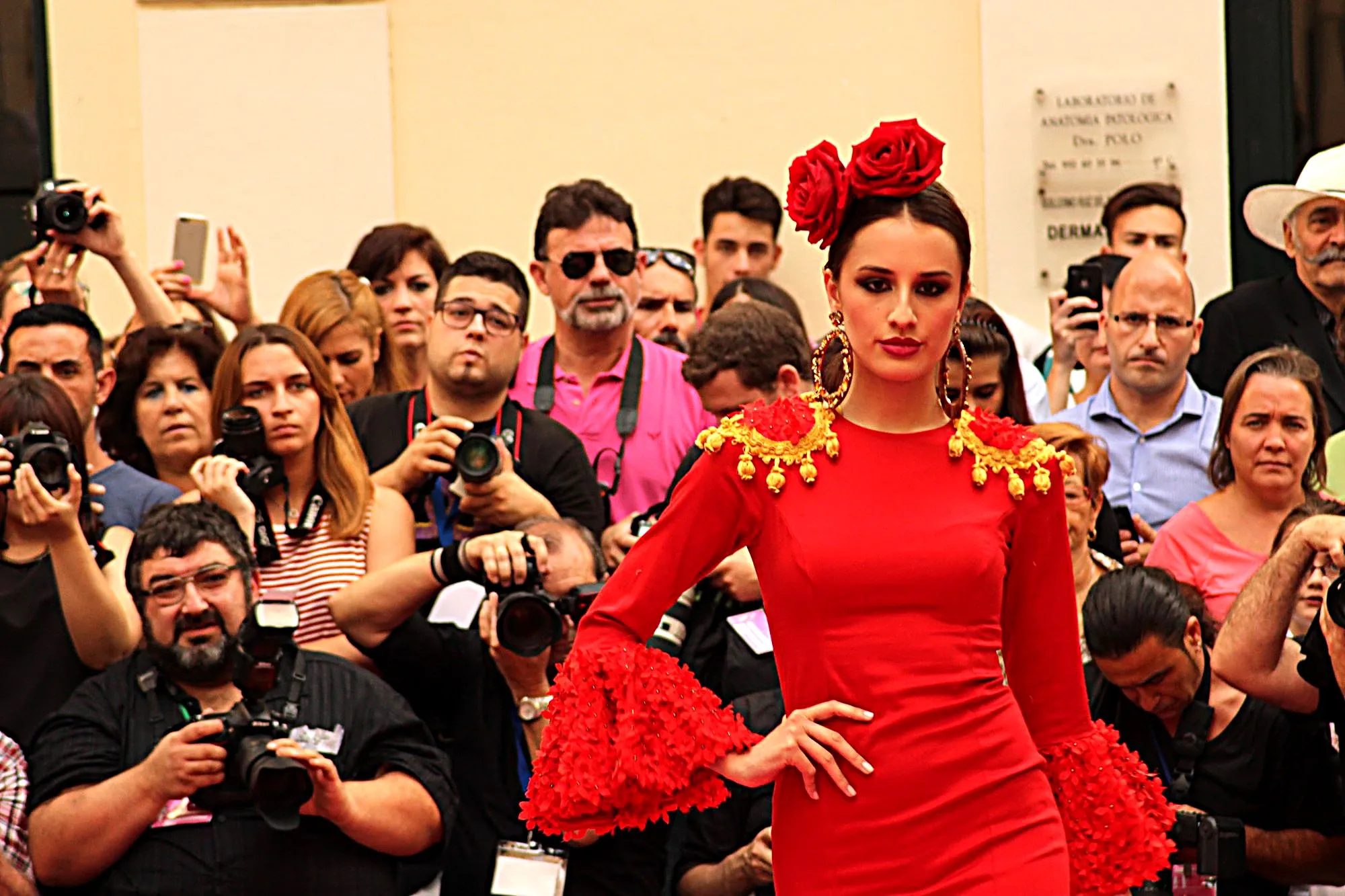 Modelo con traje de flamenca rojo, hombreras doradas y dos rosas en el pelo, ante los fotógrafos
