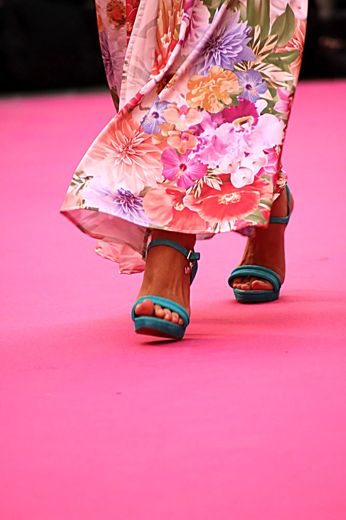 Detalle de unas sandalias turquesa y el bajo de un vestido de flores sobre la alfombra rosa