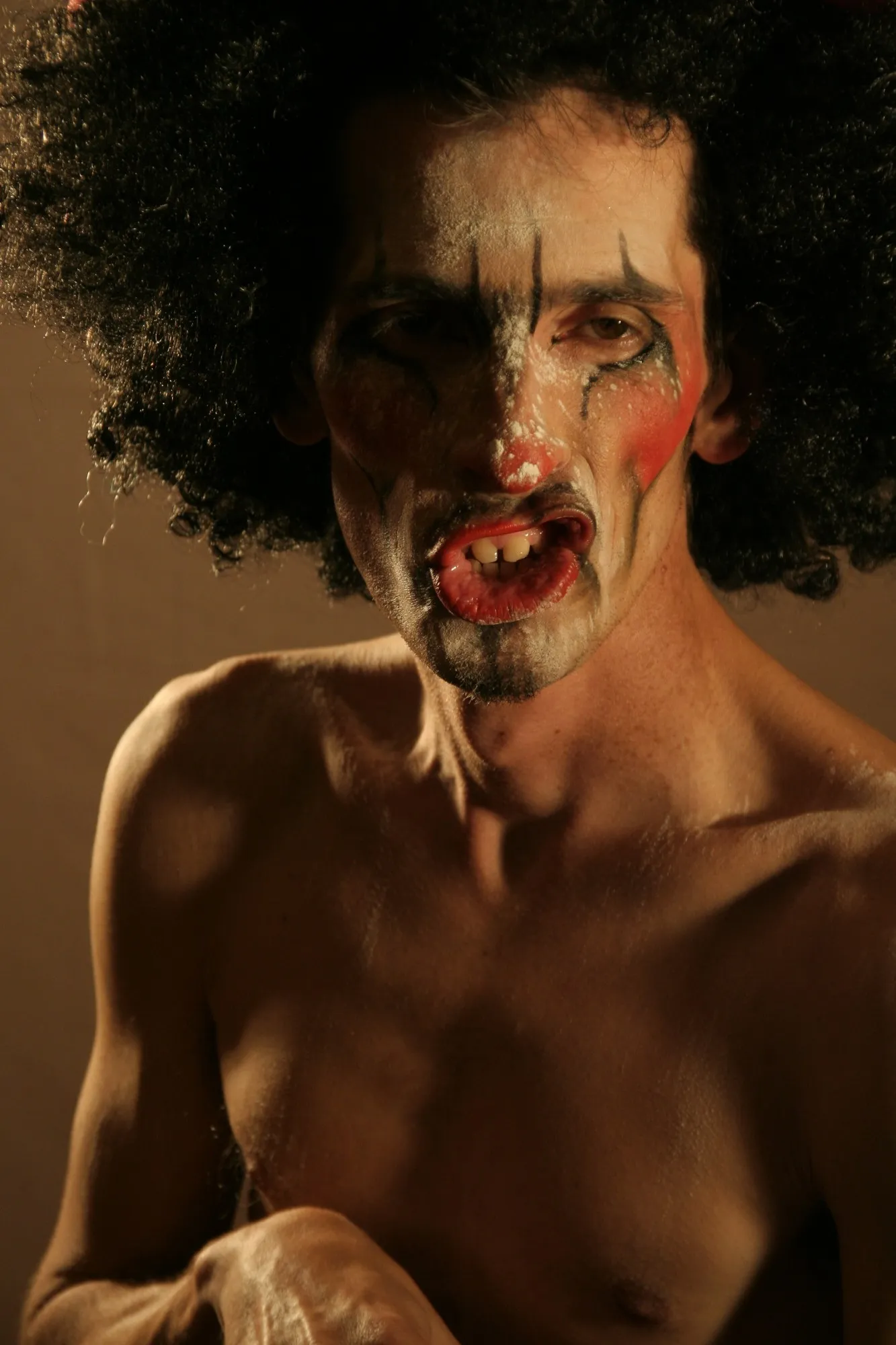 Retrato de un actor con maquillaje de payaso y peluca afro, sobre fondo cálido