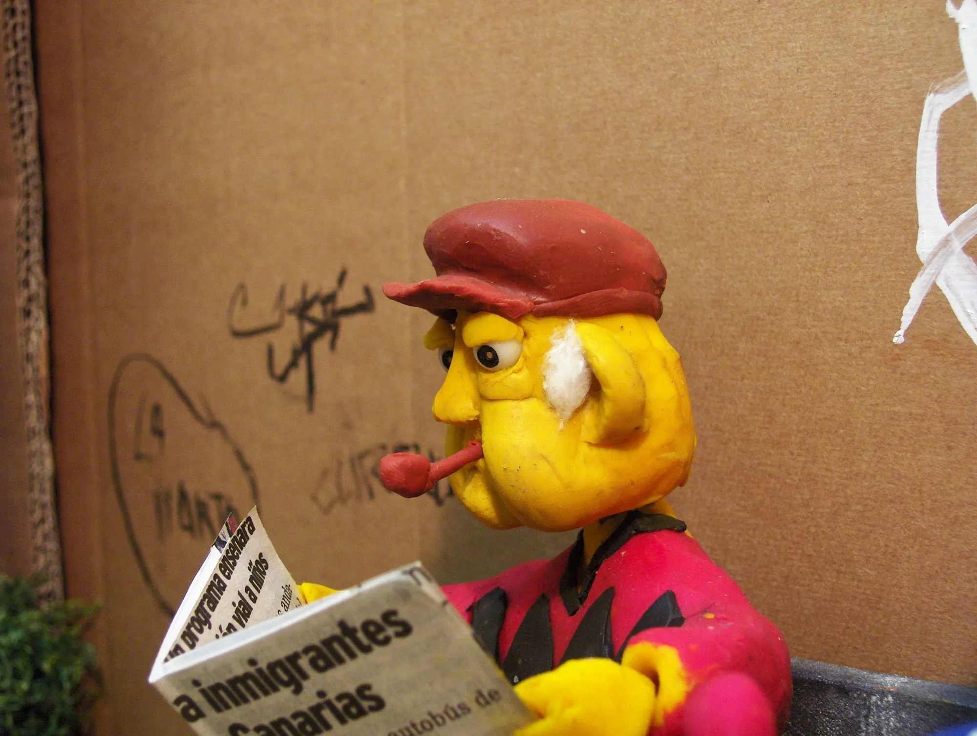 Perfil del anciano de plastilina con gorra y pipa leyendo el periódico
