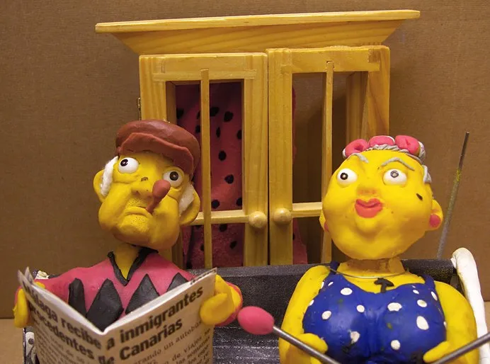 La pareja de ancianos de plastilina en el banco, él leyendo el periódico, ante una ventana de madera con cortina de lunares