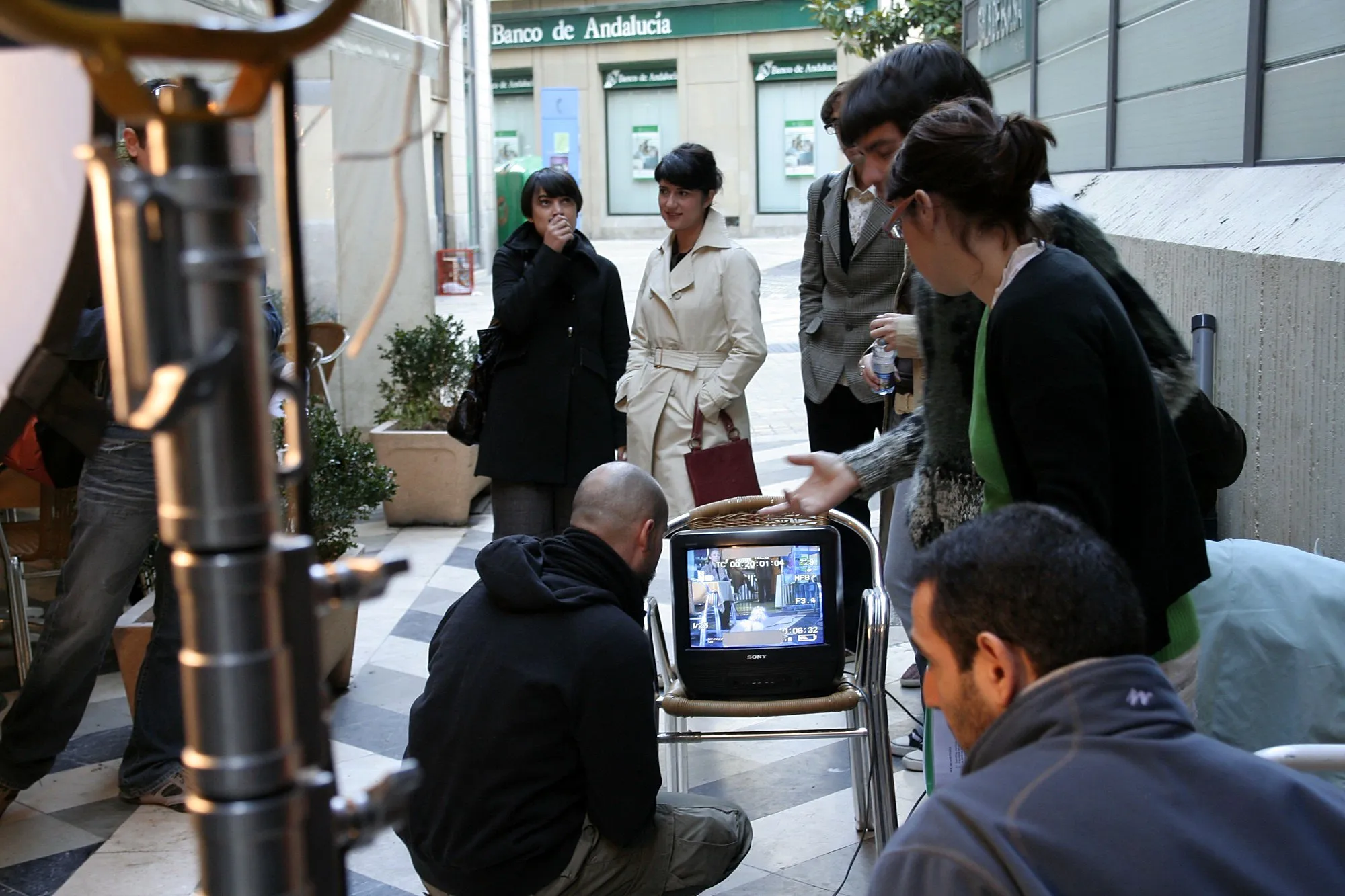 Equipo y actrices revisando una toma en un monitor colocado en una silla de terraza, en una calle del centro