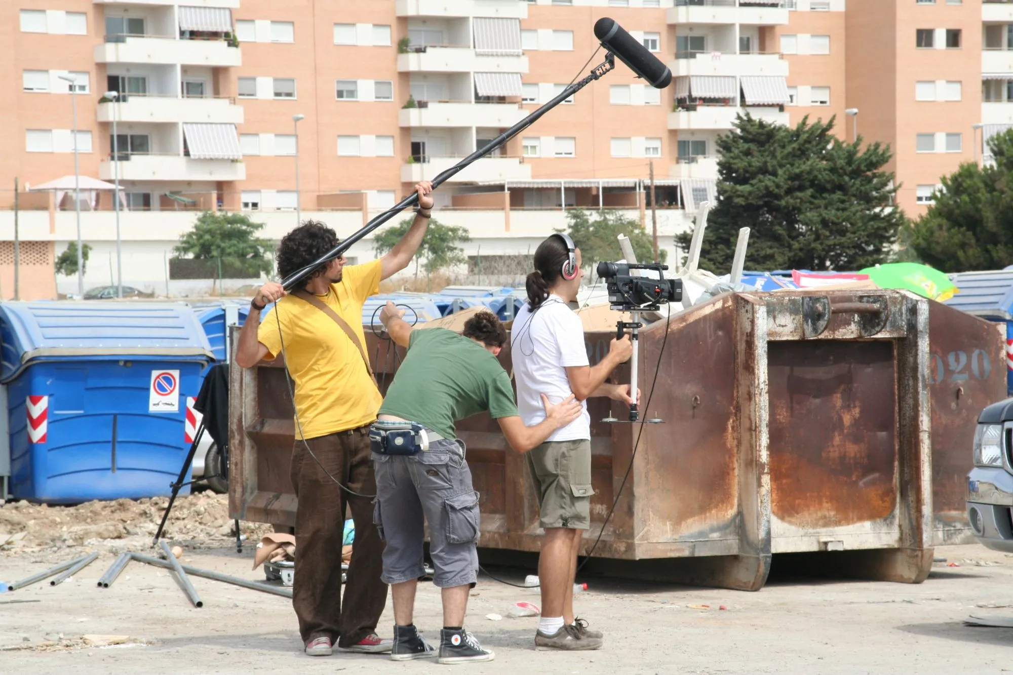 Equipo de rodaje con pértiga de sonido y cámara grabando junto a un contenedor oxidado