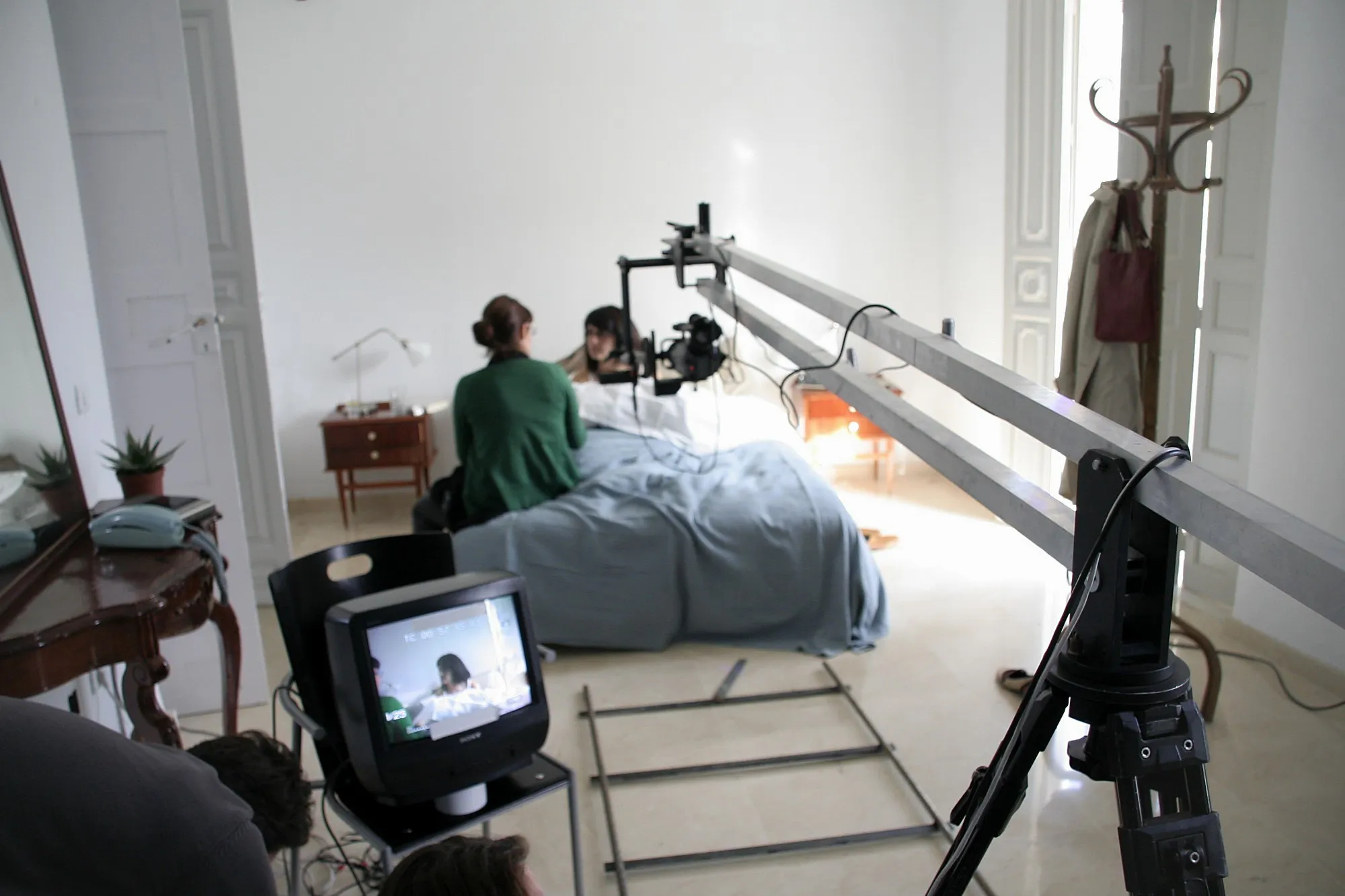 Rodaje en un dormitorio: la cámara en la punta de una grúa, la vía de travelling en el suelo y el monitor junto a la cama