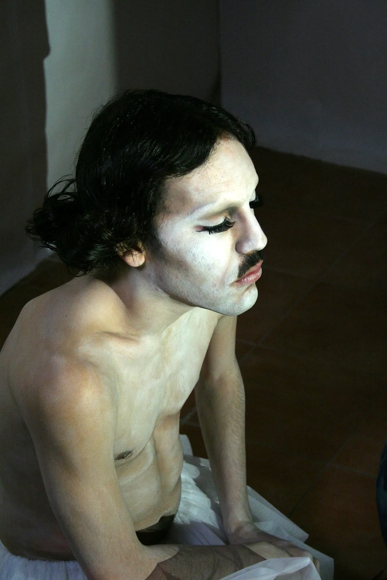 Actor con maquillaje blanco, pestañas postizas y bigote, con los ojos cerrados y luz lateral
