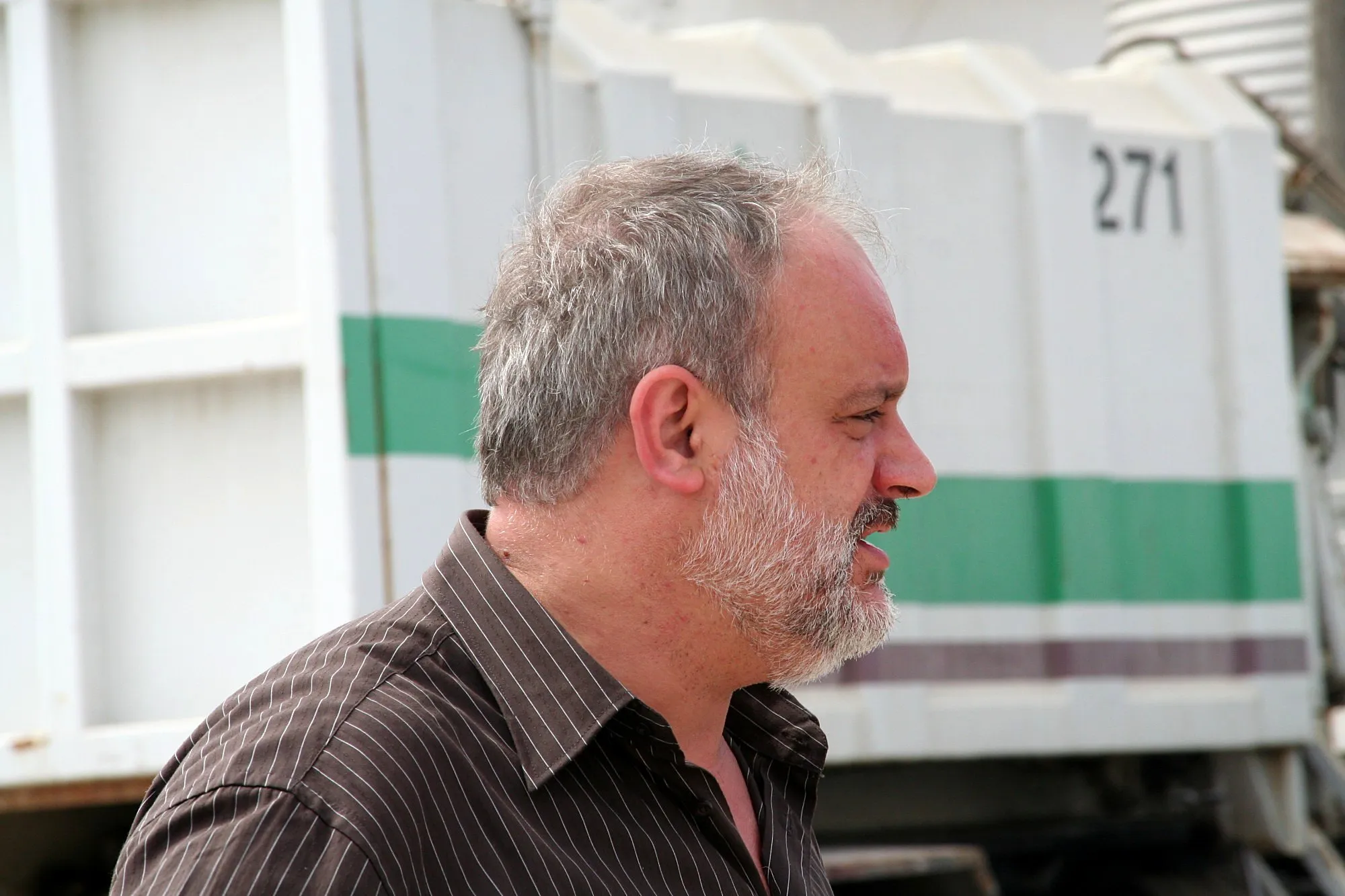 Perfil de un actor con barba gris delante de un camión de basura