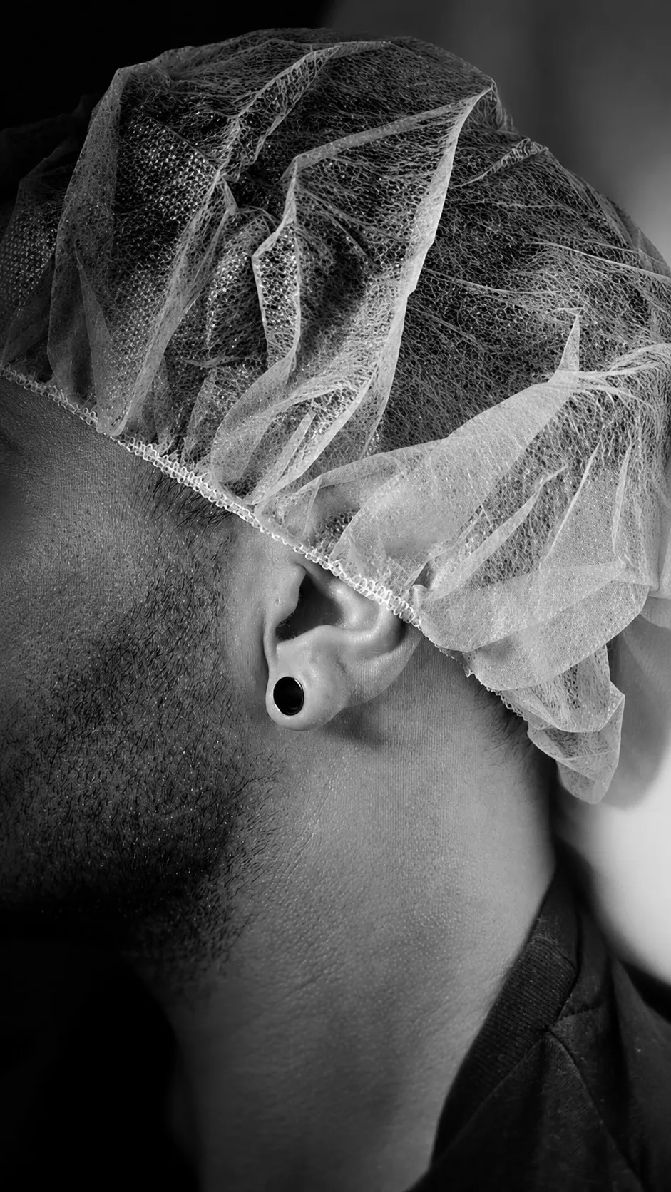Perfil de un hombre con gorro quirúrgico desechable y dilatador negro en la oreja, en blanco y negro