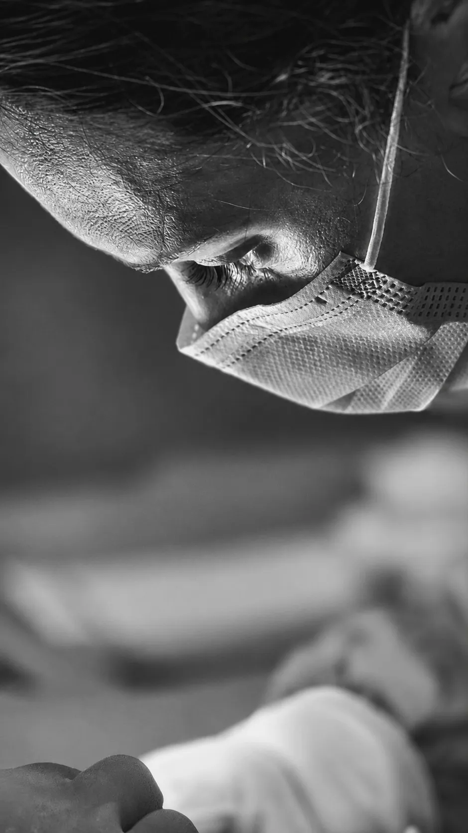 Primer plano de perfil de una cirujana con la mirada baja y la mascarilla, en blanco y negro