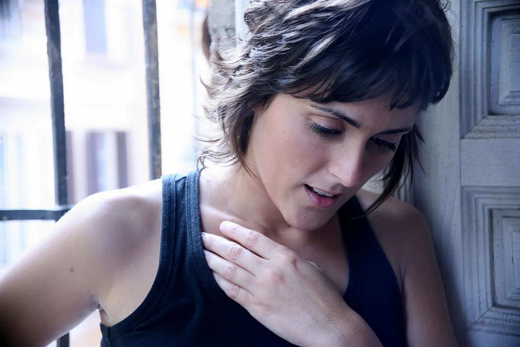 Actriz de pelo corto con camiseta negra y la mano en el pecho, junto a una ventana