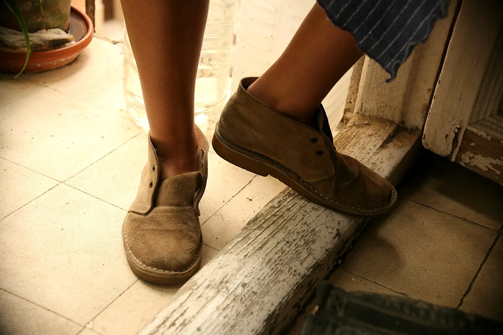 Pies con botas de ante cruzando el umbral de madera desconchada de una puerta