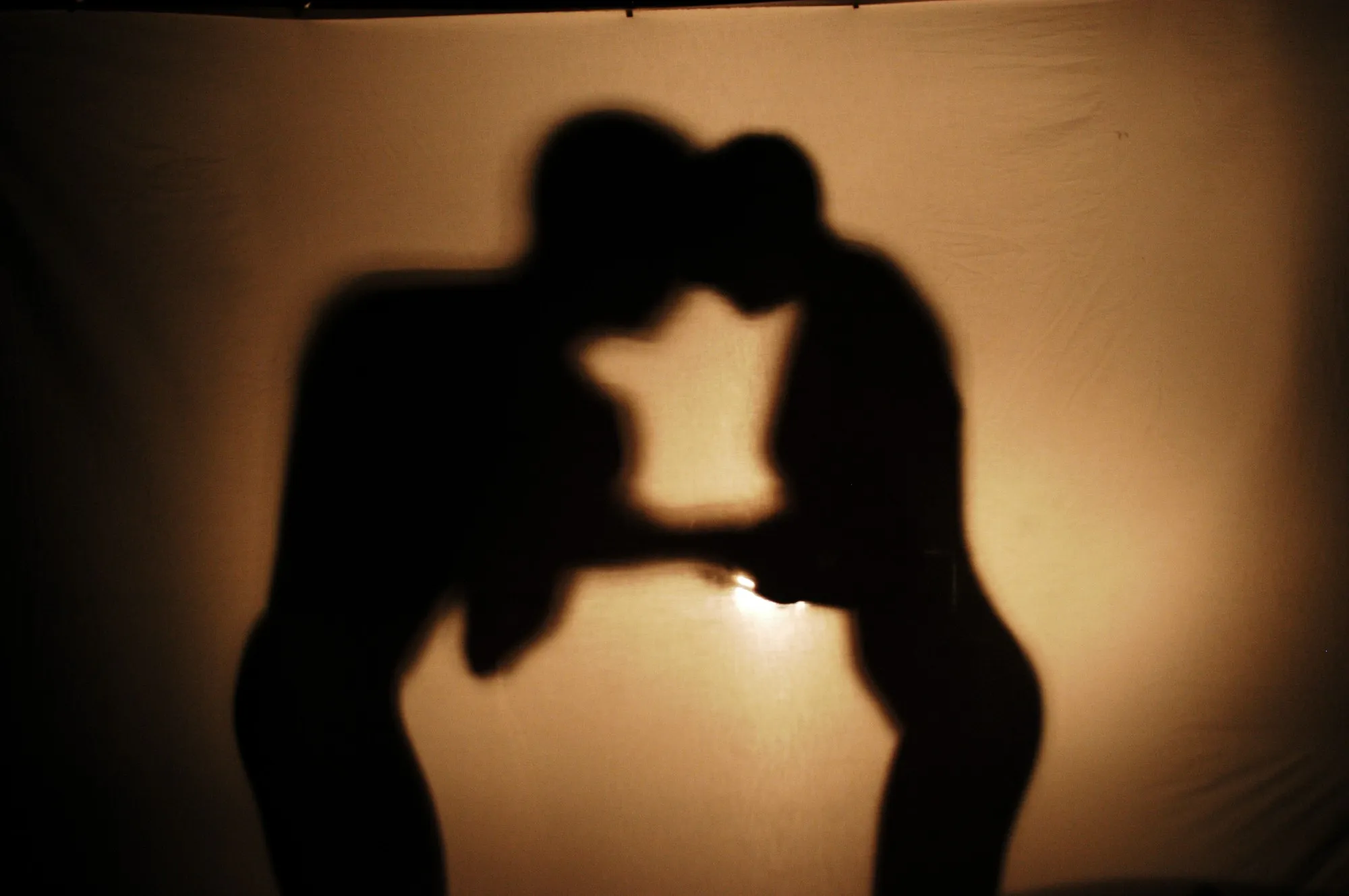 Sombras de una pareja a punto de besarse proyectadas sobre una tela iluminada