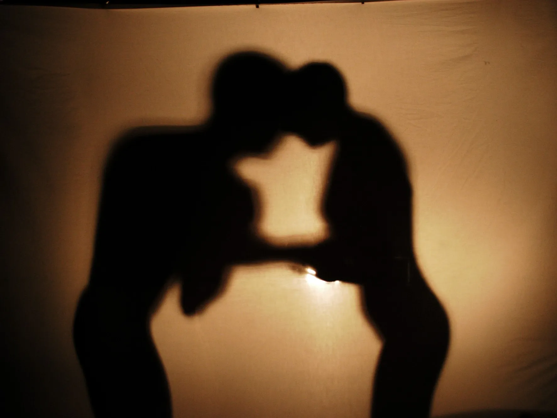 Sombras de una pareja a punto de besarse proyectadas sobre una tela iluminada