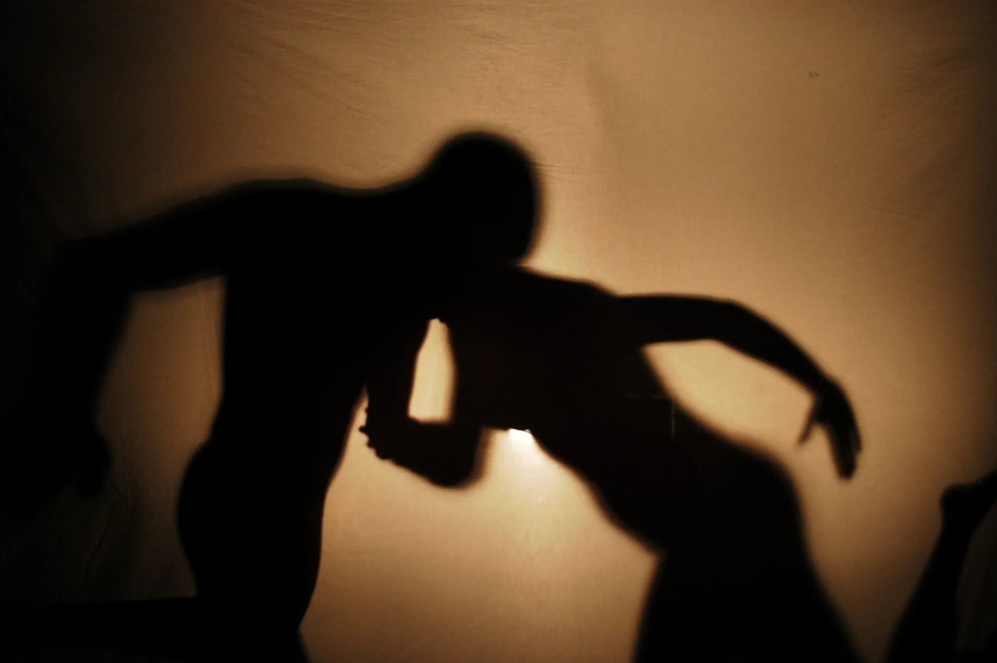 Sombras de dos bailarines en un movimiento de danza sobre una tela iluminada